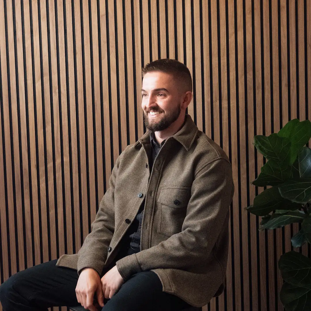 A portrait of Kyfer, a design advisor on the board of Invisaid. He is sitting on a chair with a brown coat on.